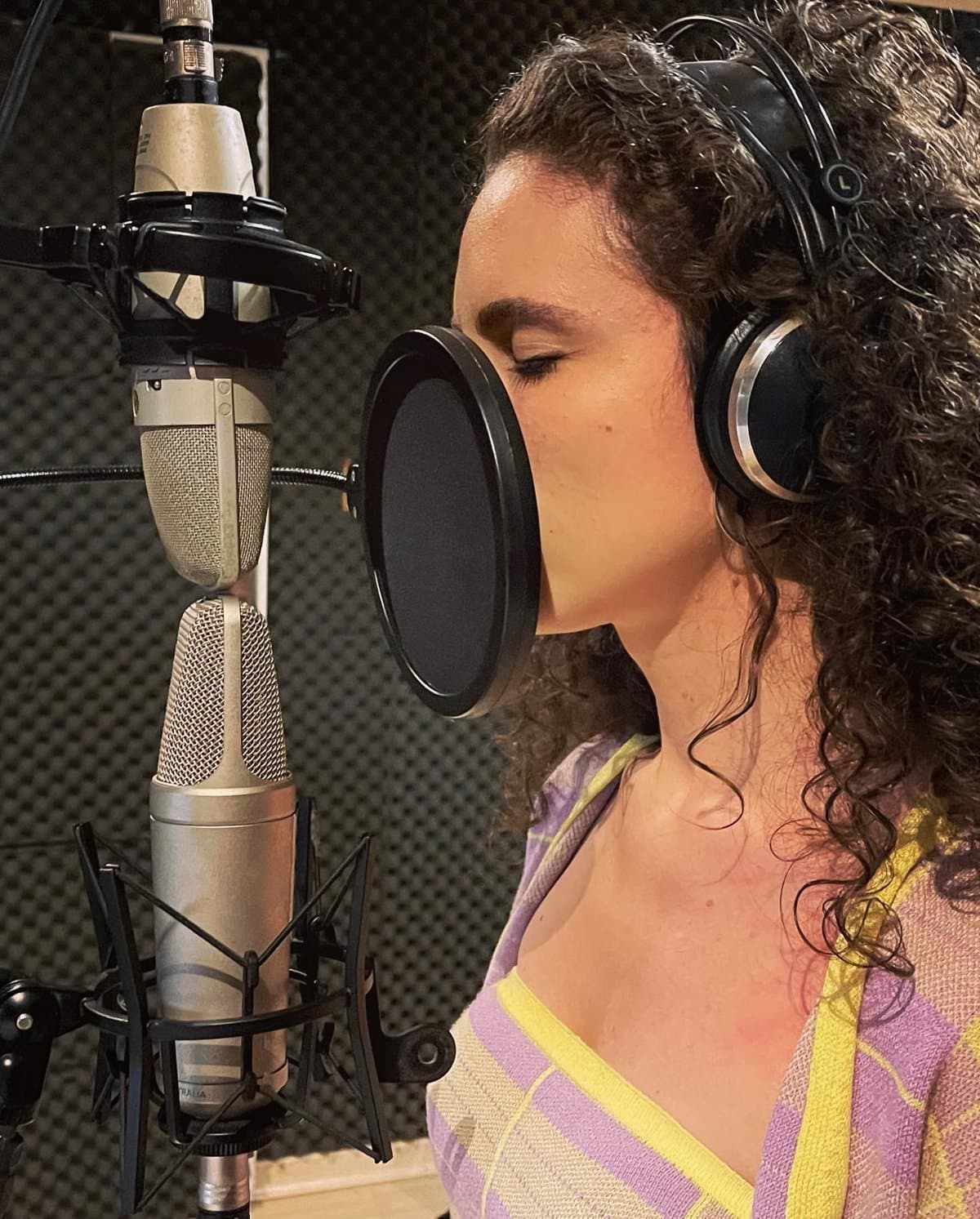 Laura Dalmás de olhos fechados gravando voz em estúdio, com microfone e fone de ouvido