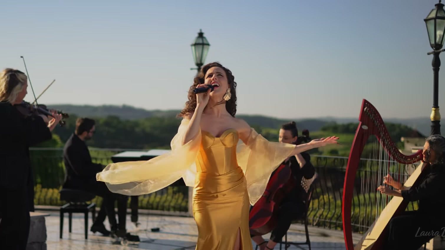 Laura Dalmás de vestido dourado cantando com o Sexteto Gold, com violino, teclado, violoncelo e harpa, em uma vinícola